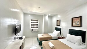 A hotel room with two beds, a desk with a computer, a TV, and a window with blinds. - Ace Penzionne (Lapu-Lapu)