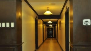 A hotel hallway with a wooden floor, dark walls, and a sign indicating WiFi availability. - Ace Penzionne (Lapu-Lapu)