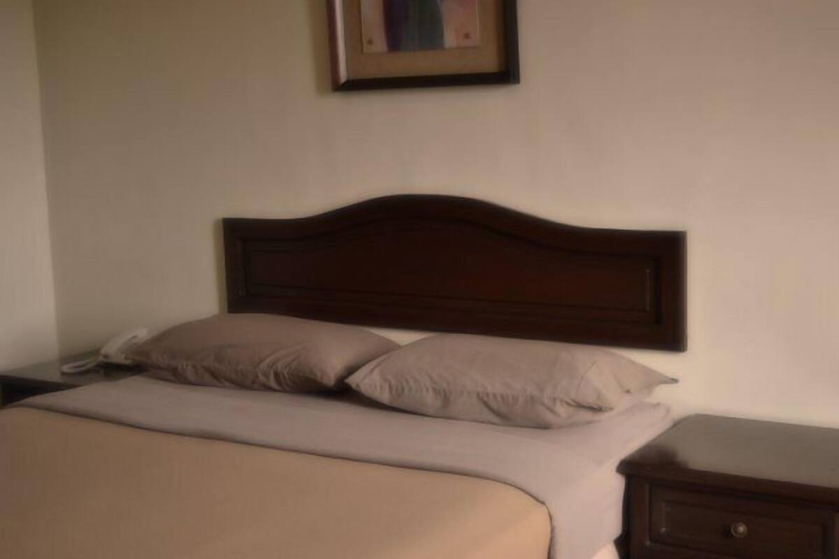 A neatly made bed with a wooden headboard, a bedside table with a lamp, and a framed picture on the wall.