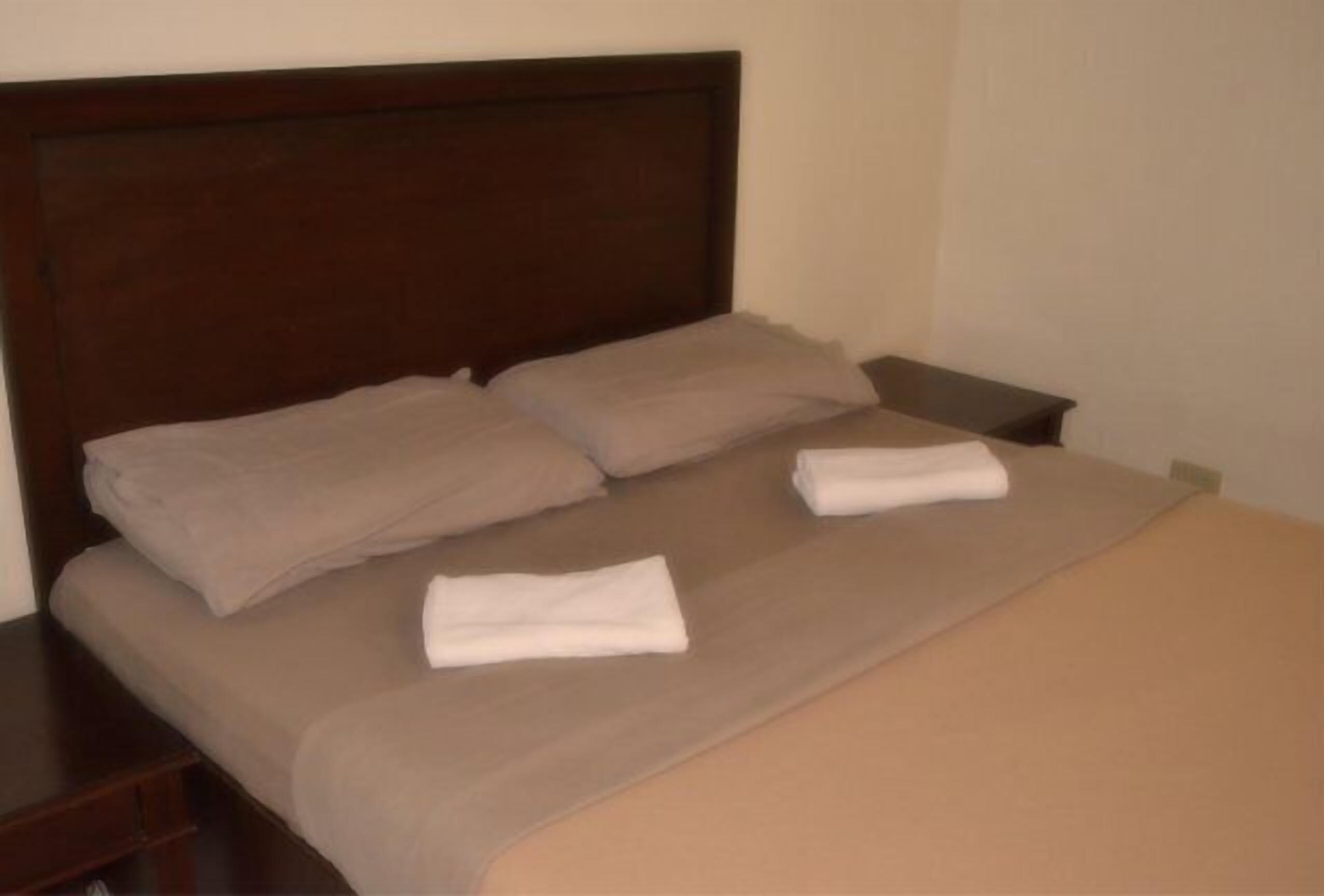 Un lit bien fait, avec une tête de lit en bois, deux oreillers et deux serviettes pliées.