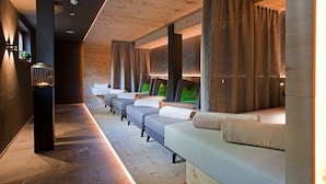 Uma fileira de cadeiras de massagem com painéis de madeira e cortinas, uma pequena mesa com uma vela, e um aplique na parede.