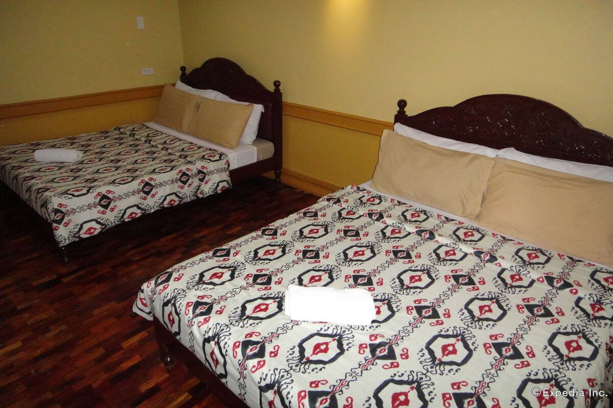 Dos camas individuales con ropa de cama estampada en una habitación con suelo de madera y paredes amarillas.