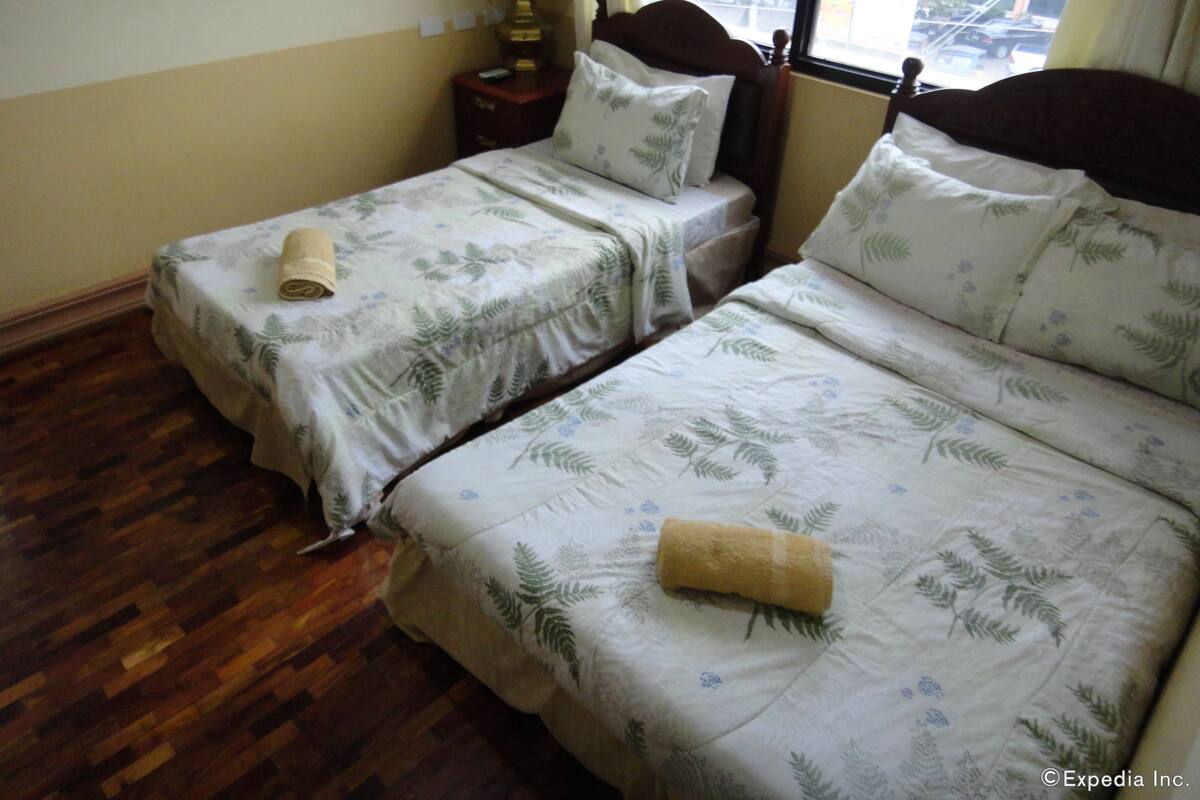 Una habitación con dos camas, cada una con cabecero de madera, una mesita de noche con lámpara y ventana con vista a la calle.