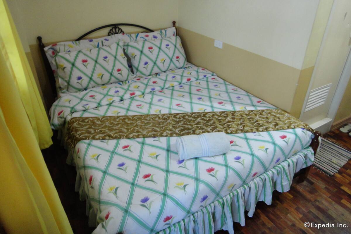 Una cama con ropa de cama floral, un cabecero de madera y una cortina amarilla.