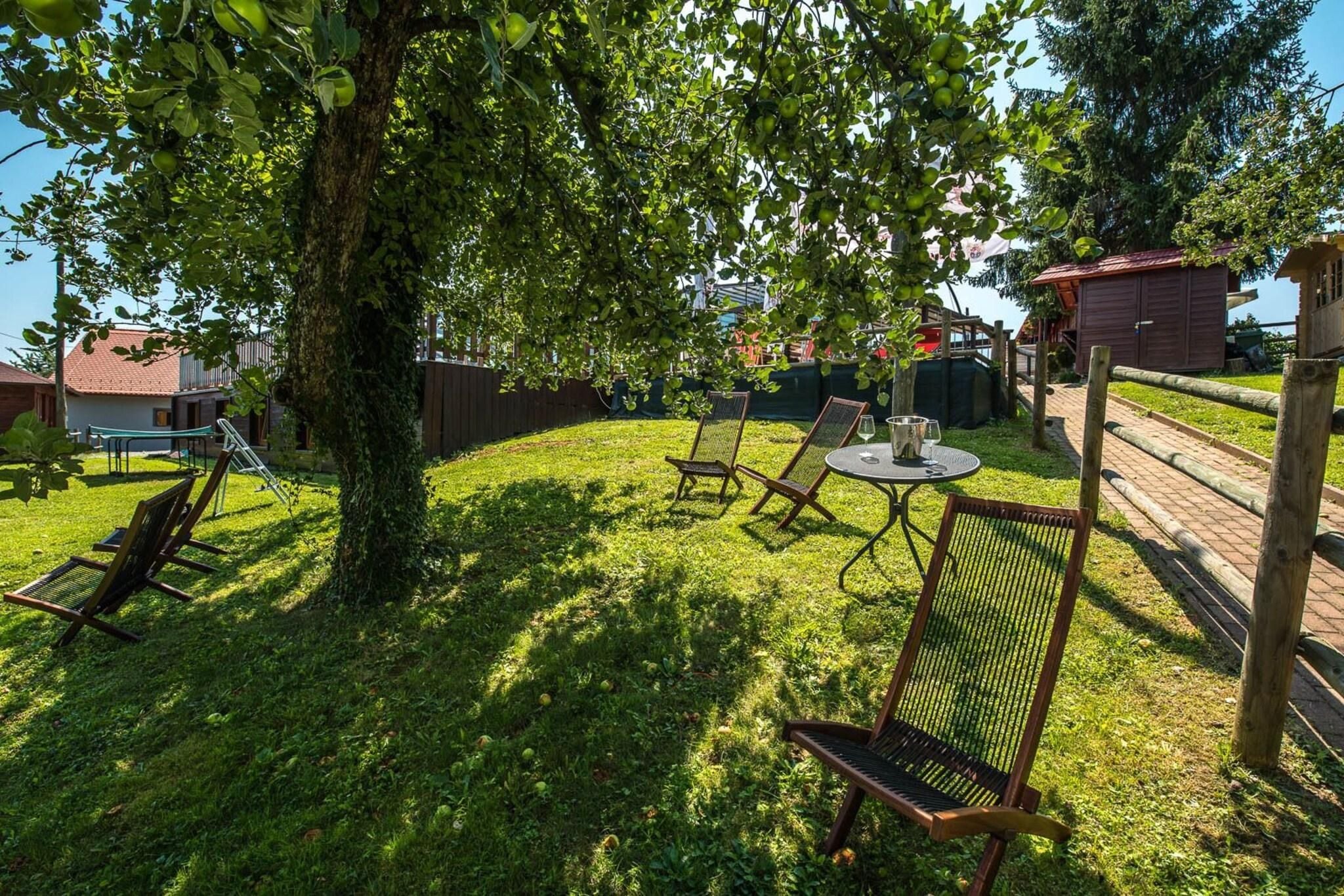 A grassy outdoor area with a tree, wooden chairs, a table, and a small building.