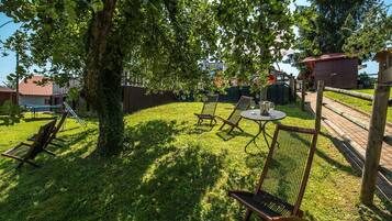 A grassy outdoor area with a tree, wooden chairs, a table, and a small building.