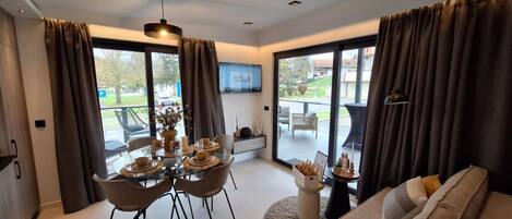 A modern living room with a dining area, large windows, and a flat-screen TV.