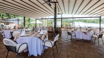 Un espacio de comedor al aire libre con mesas cubiertas con manteles blancos, sillas de metal y un ventilador de techo.
