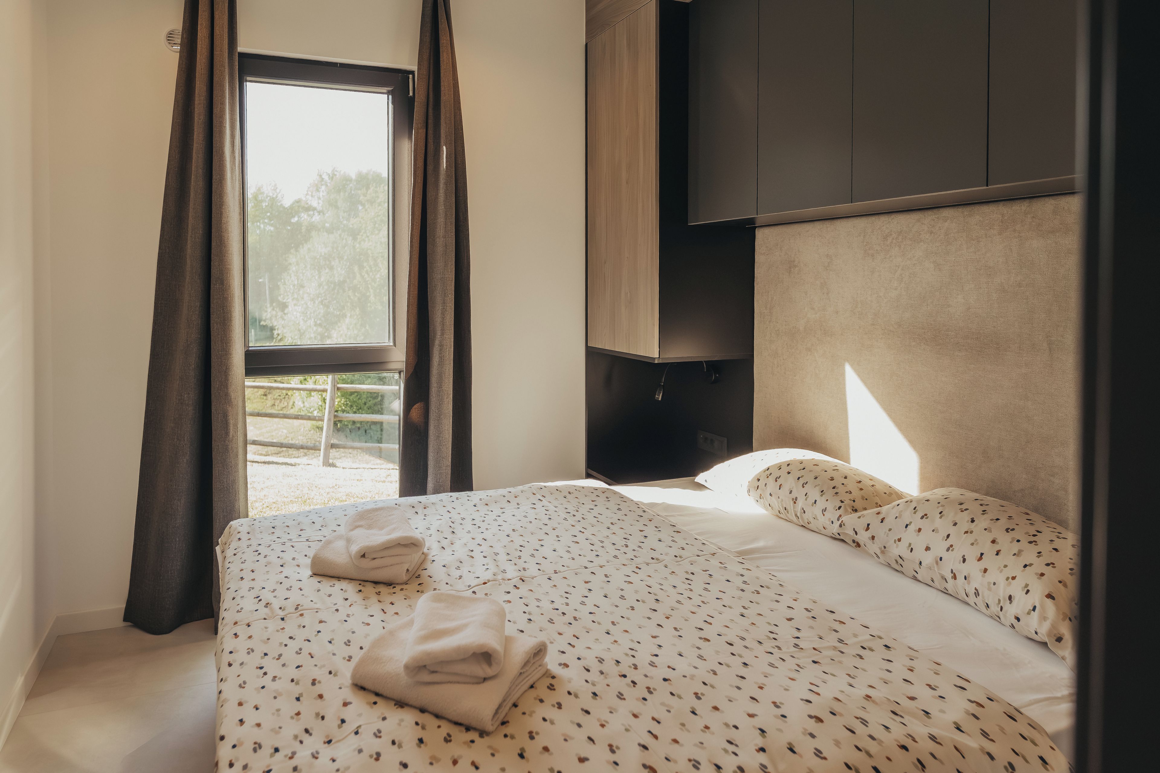 Habitación de hotel con cama, ventana con cortinas, armario y vistas al exterior.