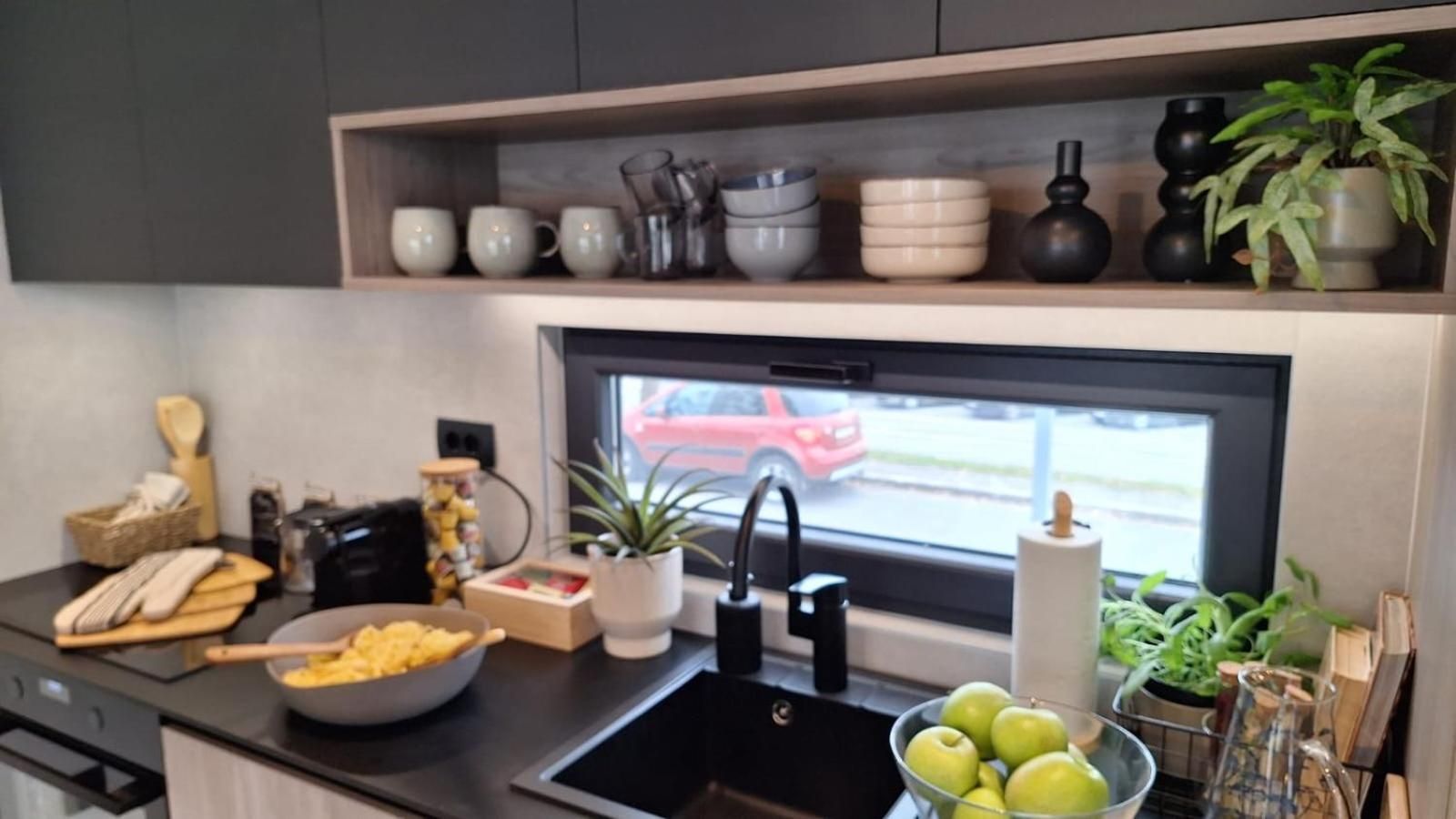 Une cuisine moderne avec un plan de travail noir, un évier et une fenêtre donnant sur une voiture rouge garée à l’extérieur.