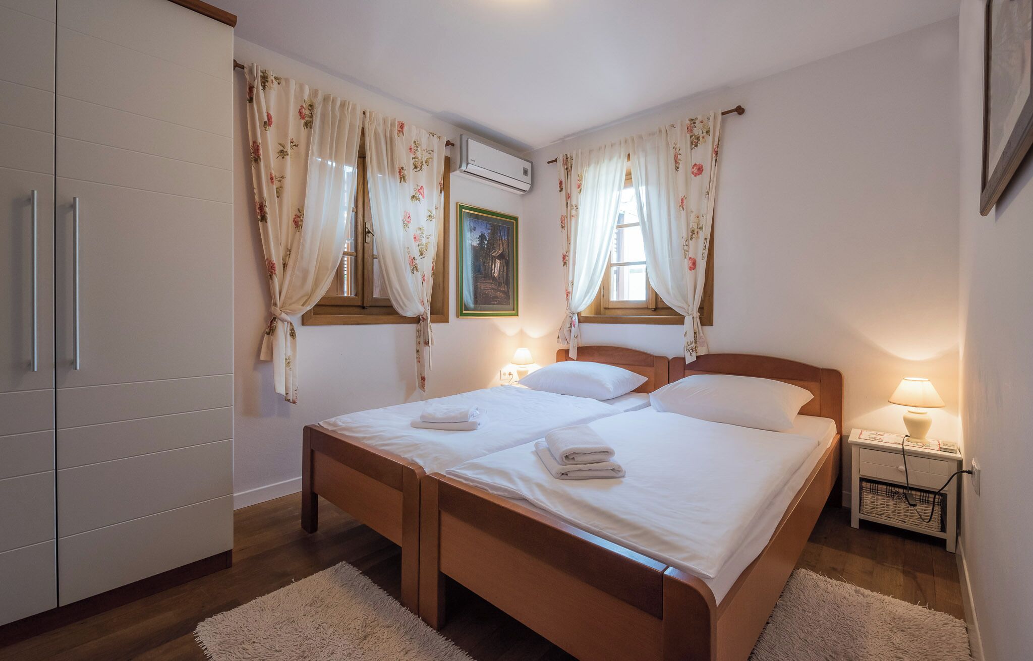 A bedroom with a double bed, a bedside table with a lamp, a wardrobe, and floral curtains.