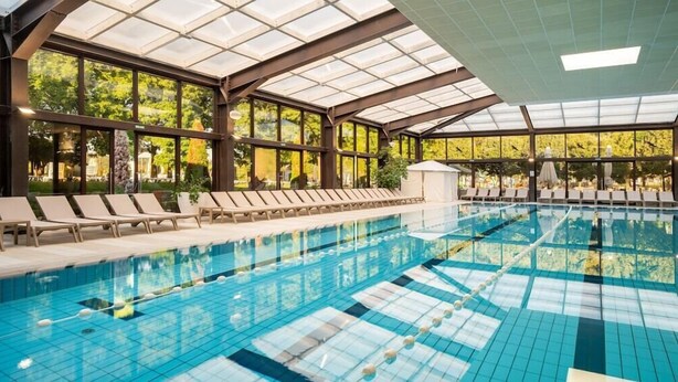 Une piscine intérieure à l’eau claire, entourée de chaises longues et dotée de grandes fenêtres.