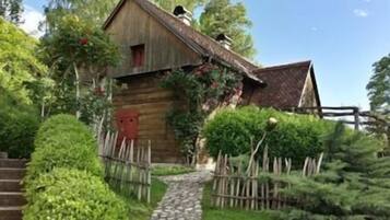 Un bâtiment rustique en bois, auquel mène un chemin de pierres, entouré de verdure et délimité par une clôture en bois.
