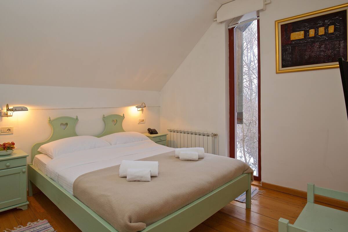 A bedroom with a bed, bedside tables, a nightstand, a radiator, and a window with a view.