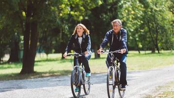 Deux personnes font du vélo sur un chemin de gravier dans un parc, au milieu des arbres.
