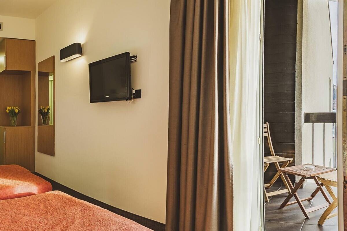 A hotel room with a bed, a flat-screen TV, a mirror, and a view of the outside.