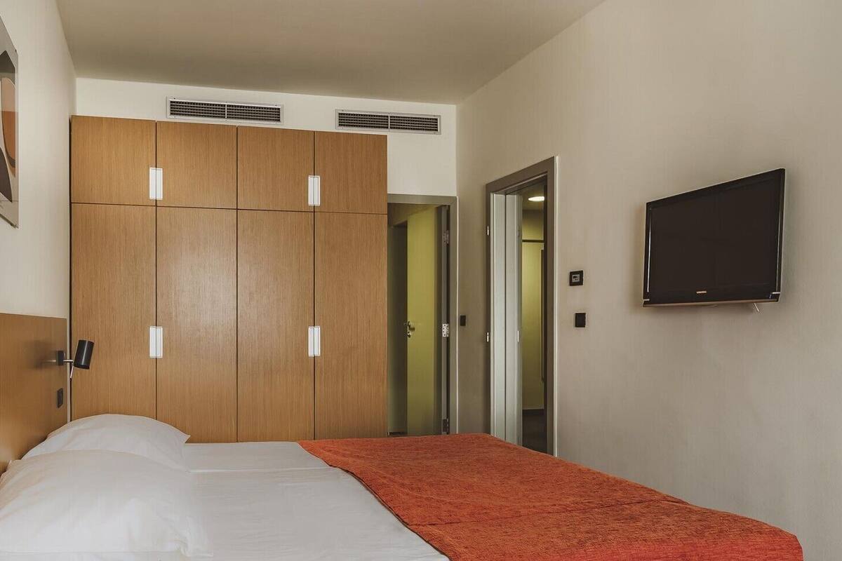 A hotel room with a bed, a wardrobe, a television, and a door leading to another room.