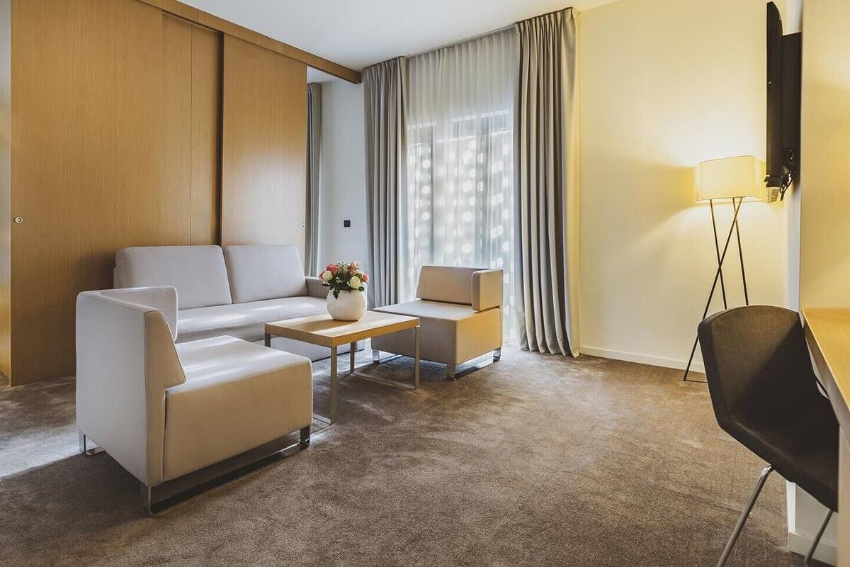 A hotel room with a sofa, two armchairs, a coffee table, a desk, and a lamp.
