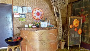 Un espace bar avec un comptoir, des certificats, un mur décoratif, un saladier de fruits et un présentoir en métal orné de motifs solaires.