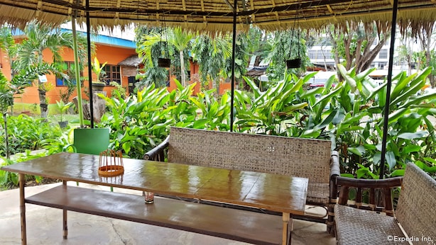 Un espace extérieur aménagé avec un banc en osier et une table, entouré d’une végétation tropicale luxuriante.