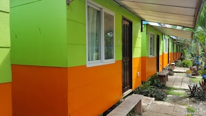Une rangée de maisons aux couleurs vives, avec des murs verts et orange, une allée couverte et un espace jardin agrémenté de plantes en pot.
