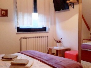 A bedroom with a bed, a radiator, a window with curtains, a small table with a vase, and a television mounted on the wall. - House Sankovic (Plitvicka Jezera)