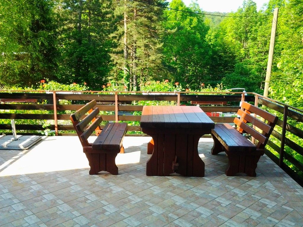 An outdoor patio with a wooden table and benches, surrounded by a wooden fence and greenery.