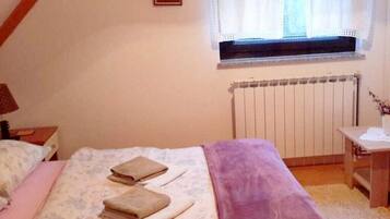 A bedroom with a bed, a window with curtains, a radiator, and a bedside table.