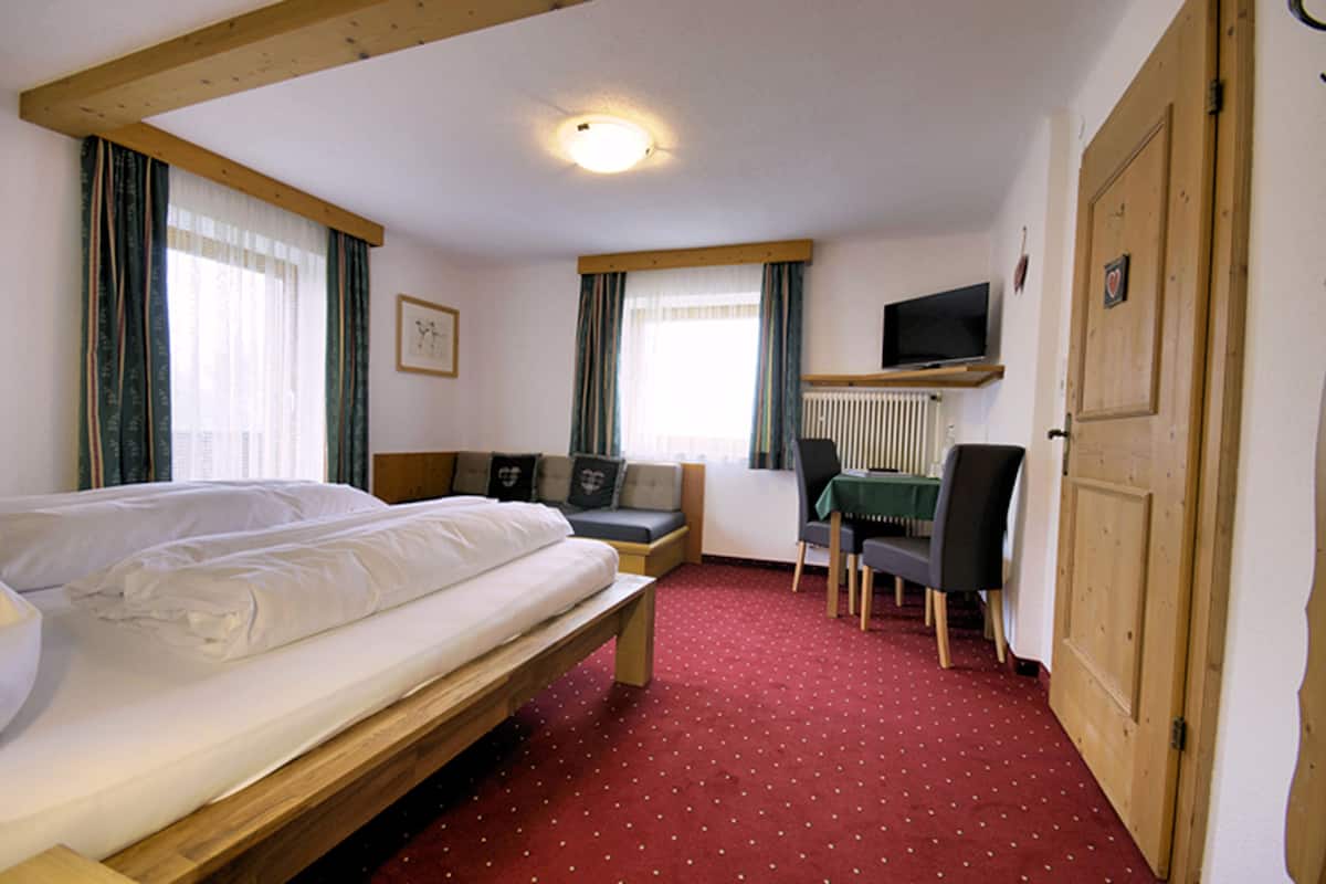 A hotel room with a bed, a small seating area, a desk, and a television.