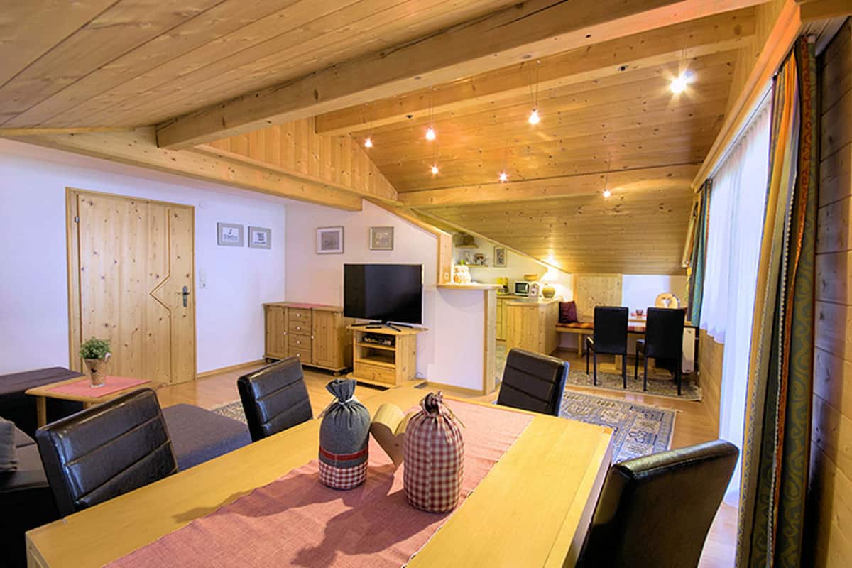 A cozy living room with a wooden ceiling, a television, and a dining area with a table and chairs.