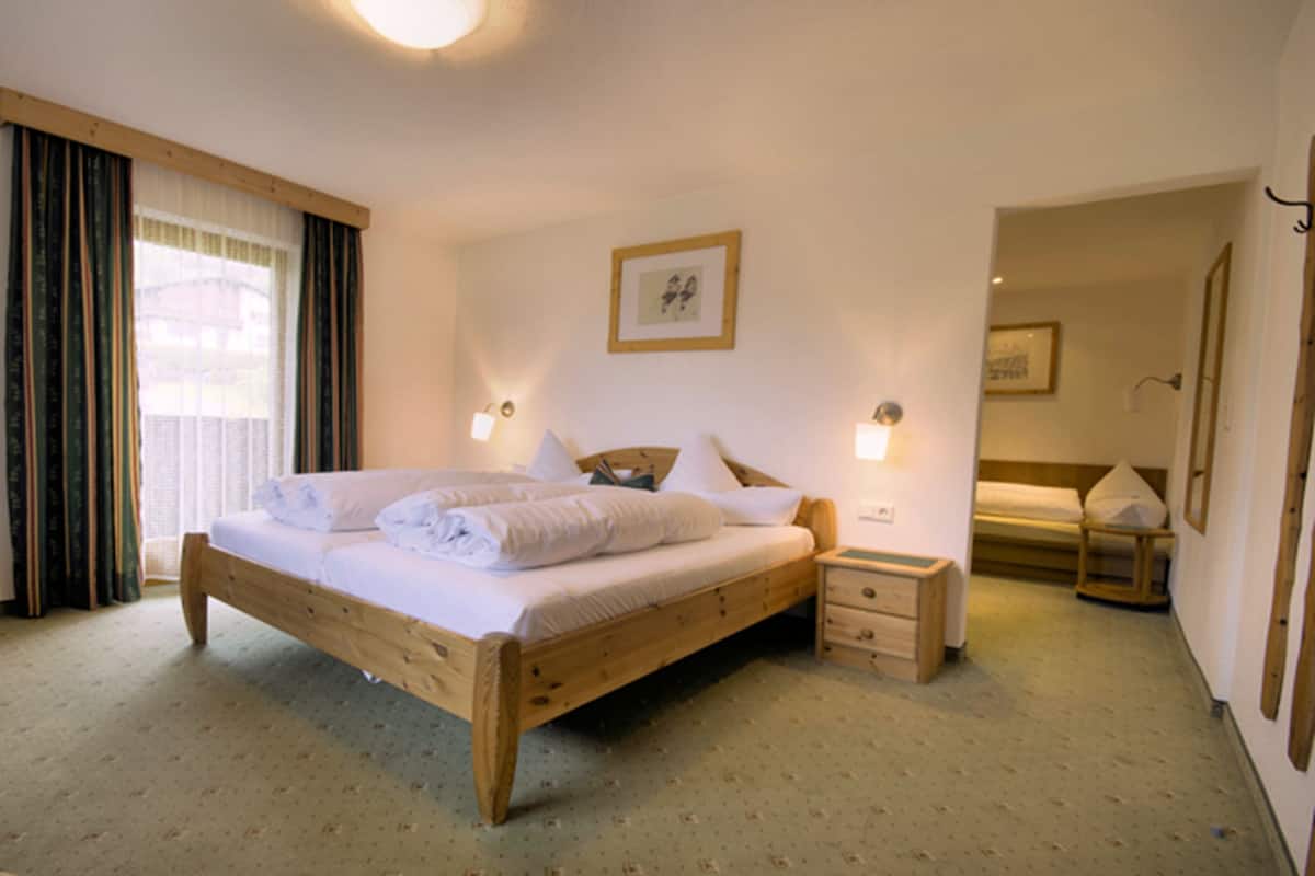 A bedroom with a wooden bed, two bedside tables, a nightstand, a window with curtains, and a framed picture on the wall.