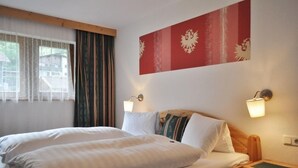 A hotel room with a bed, two bedside tables, a wall-mounted light, and a window with curtains. - Gästehaus Hackl (Sautens)