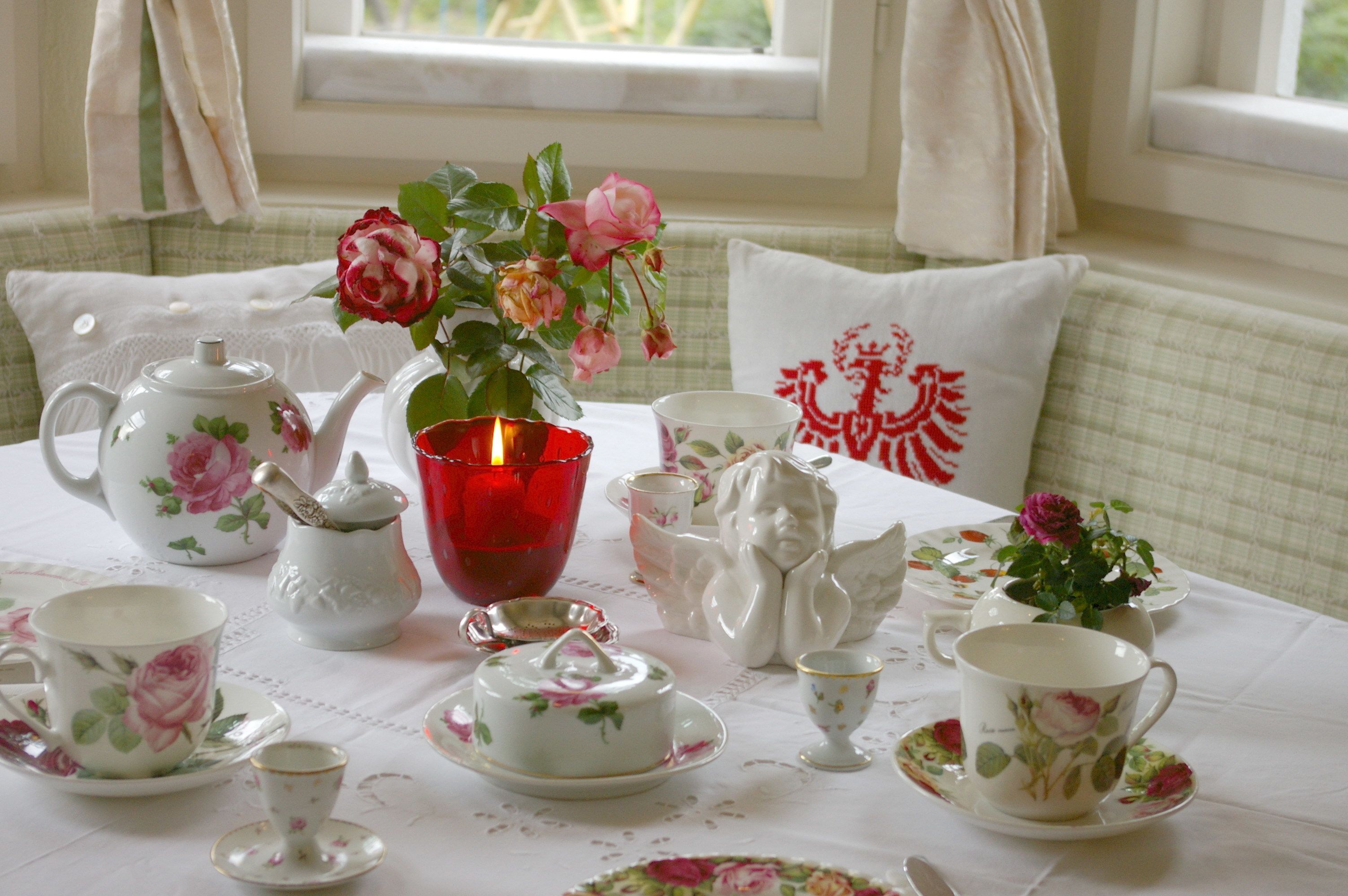 A table set with floral tea service, a red candle, and decorative items.