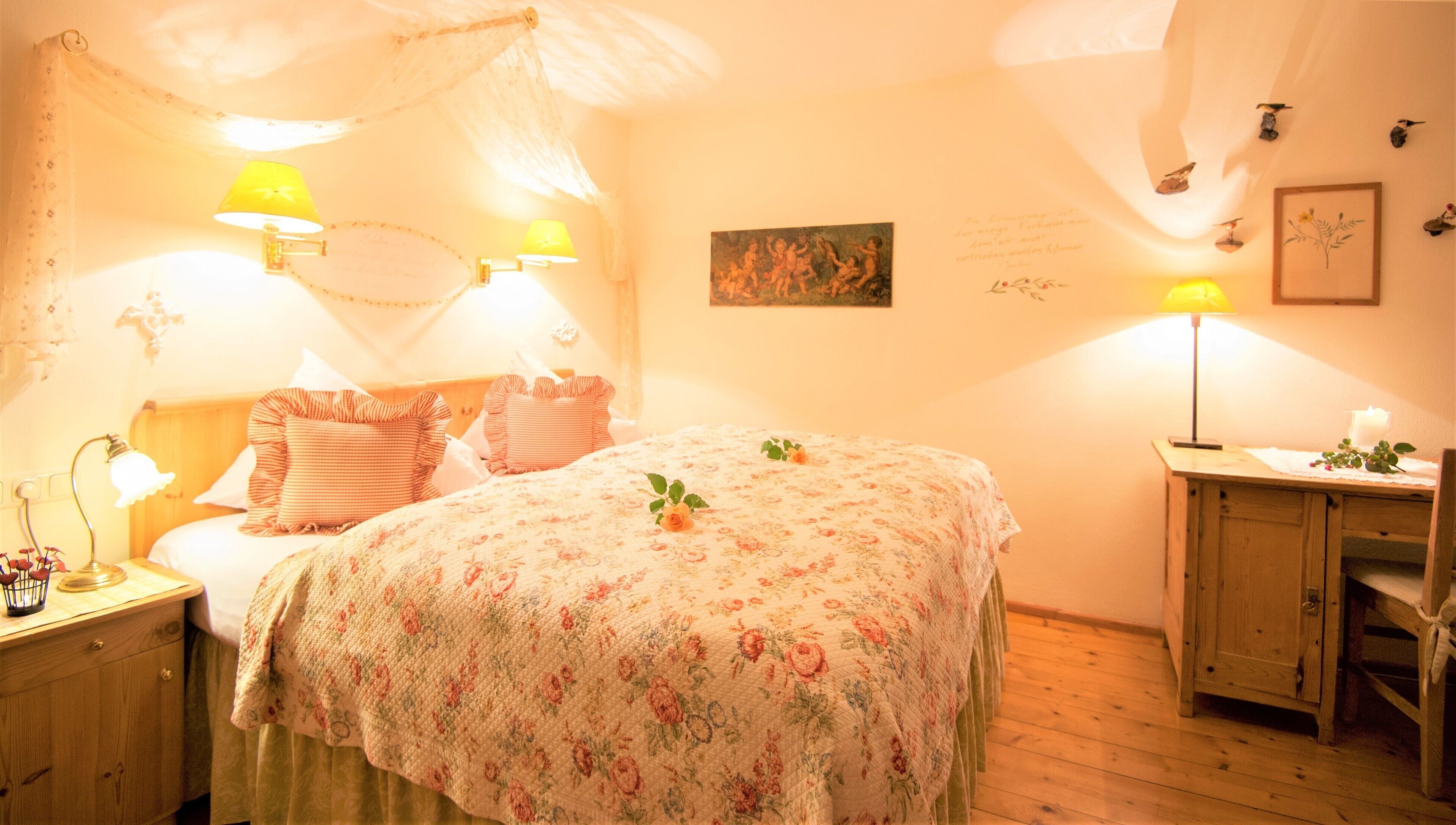 A cozy bedroom with a floral bedspread, two bedside lamps, a wooden nightstand, and a small table with a candle.