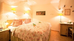 A cozy bedroom with a floral bedspread, two bedside lamps, a wooden nightstand, and a small table with a candle. - Haus Alpengruss (Seefeld in Tirol)