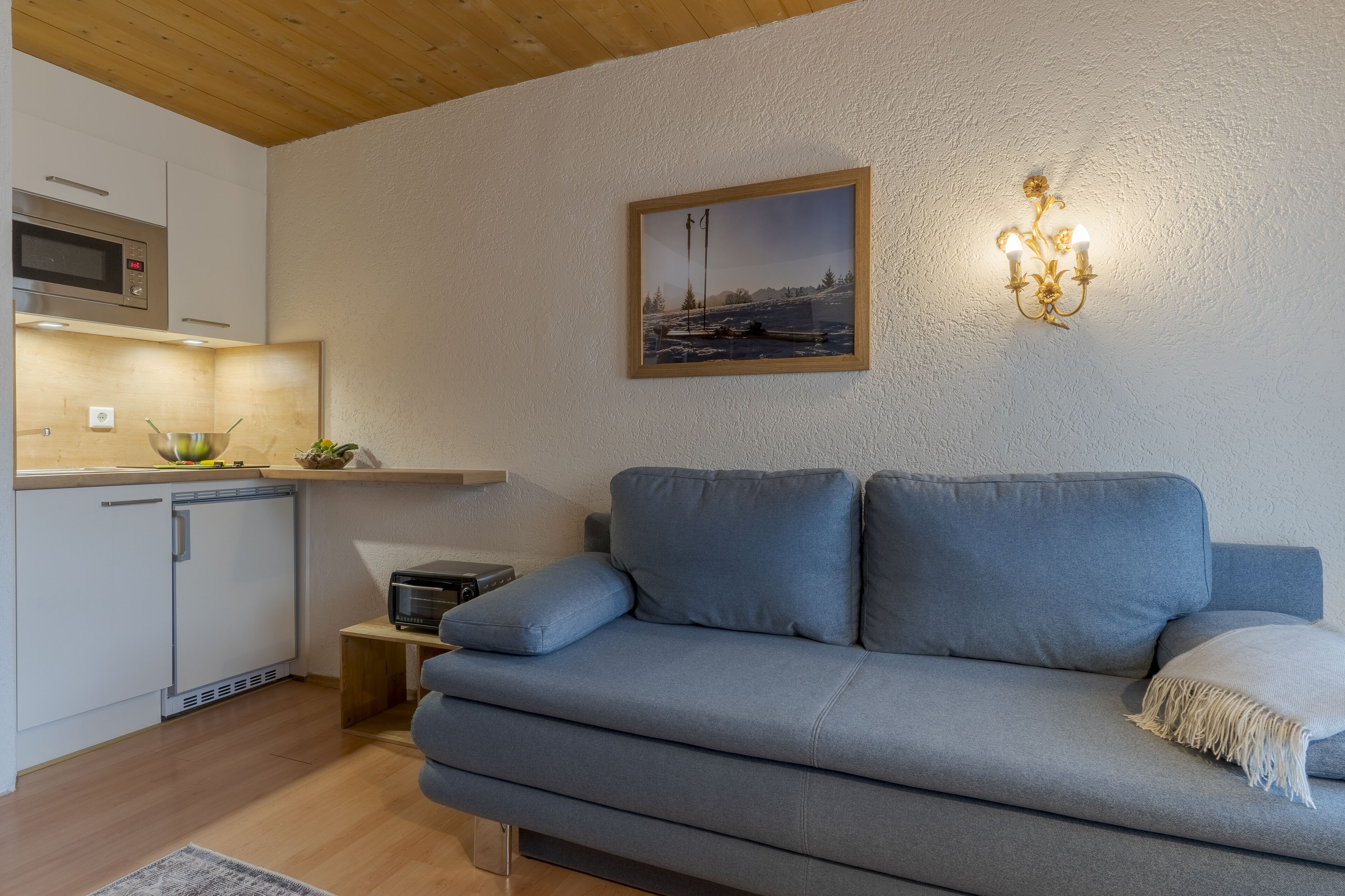 A modern living room with a grey sofa, a small side table, a microwave, and a framed picture on the wall.