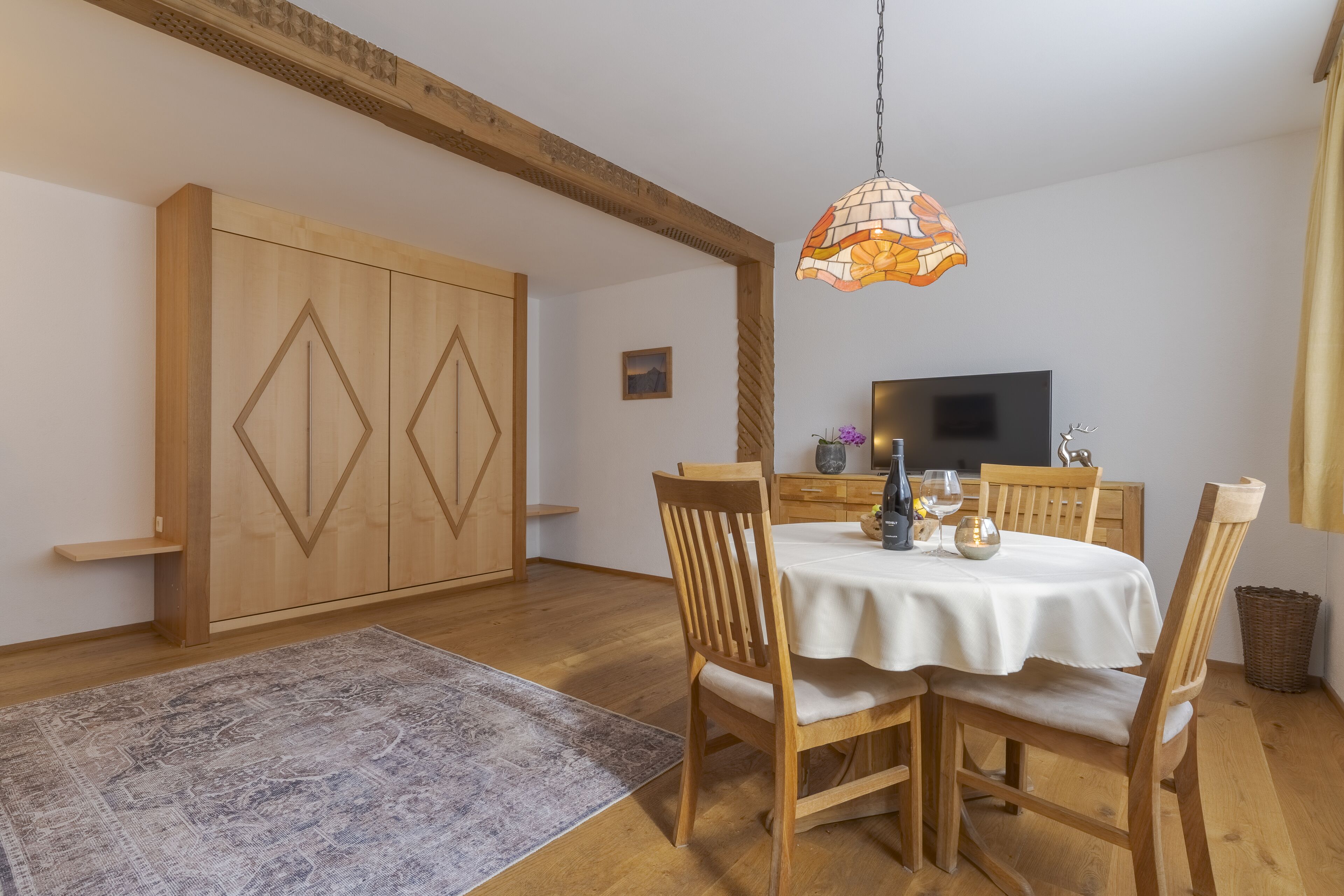Een eethoek met een houten tafel en stoelen, een kamerbreed tapijt en een hanglamp.