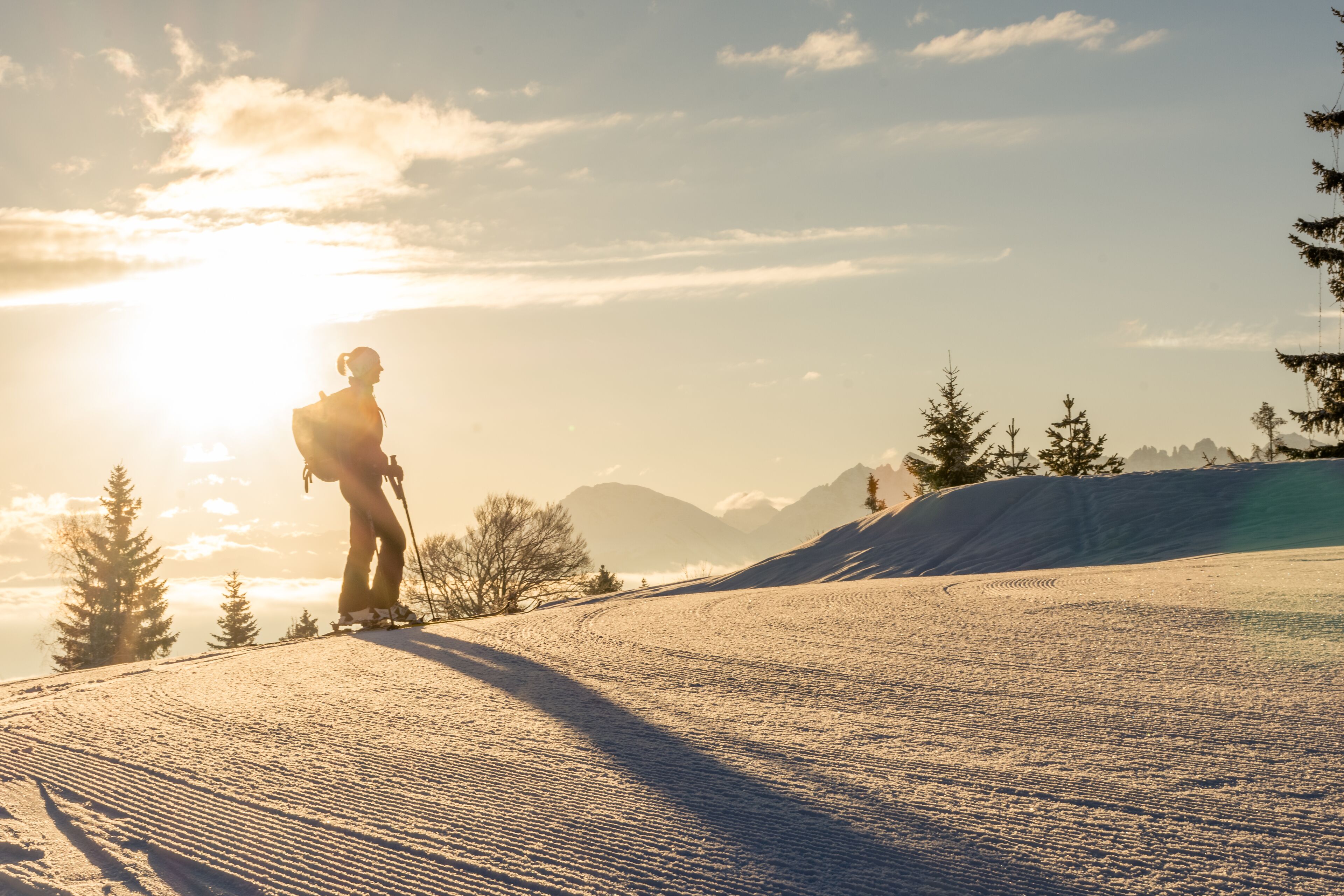 A person skiing on a snowy slope with a clear sky and mountains in the background.