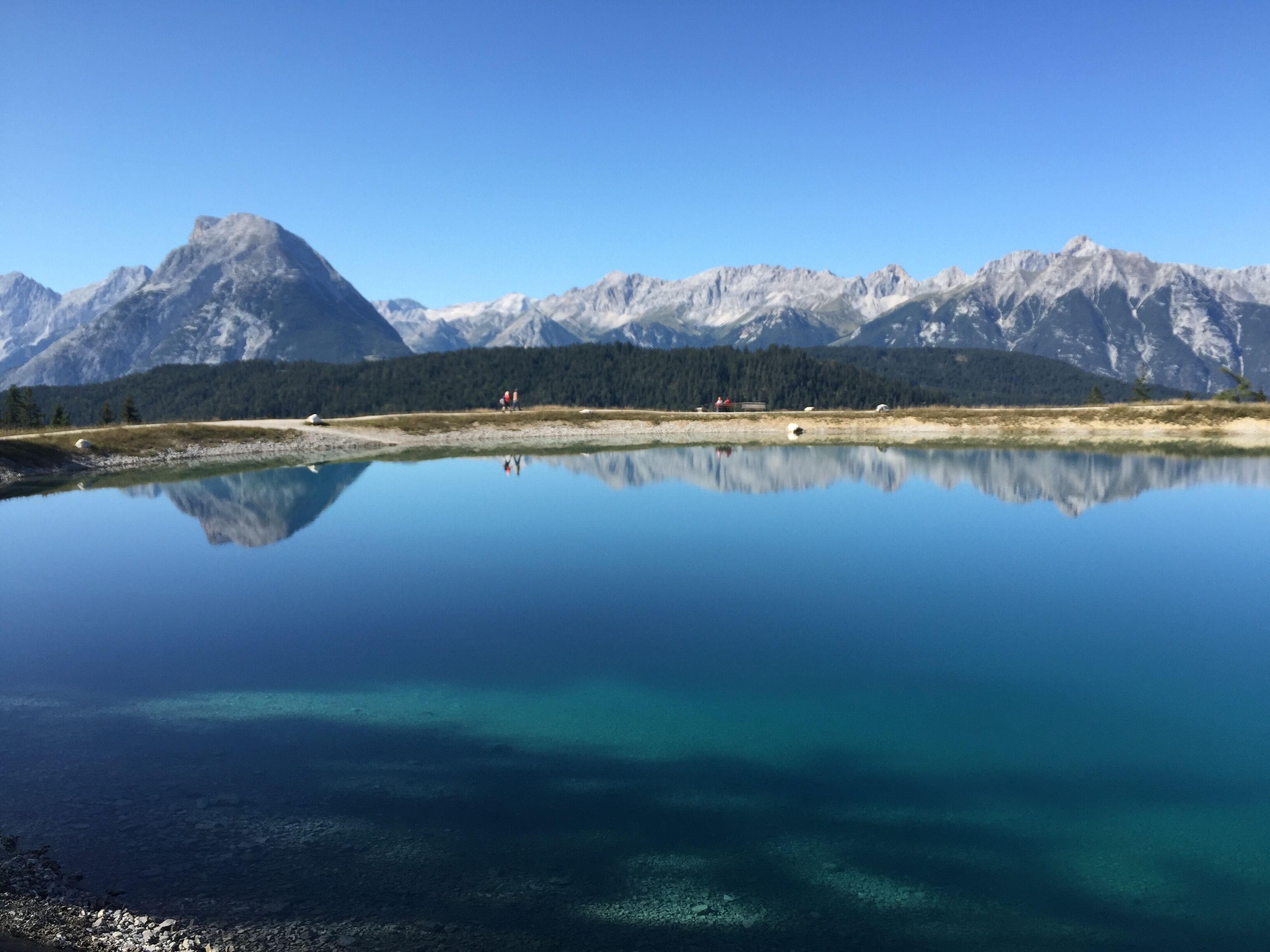Un lago tranquillo con riflessi chiari di montagne lontane e una zona boschiva.