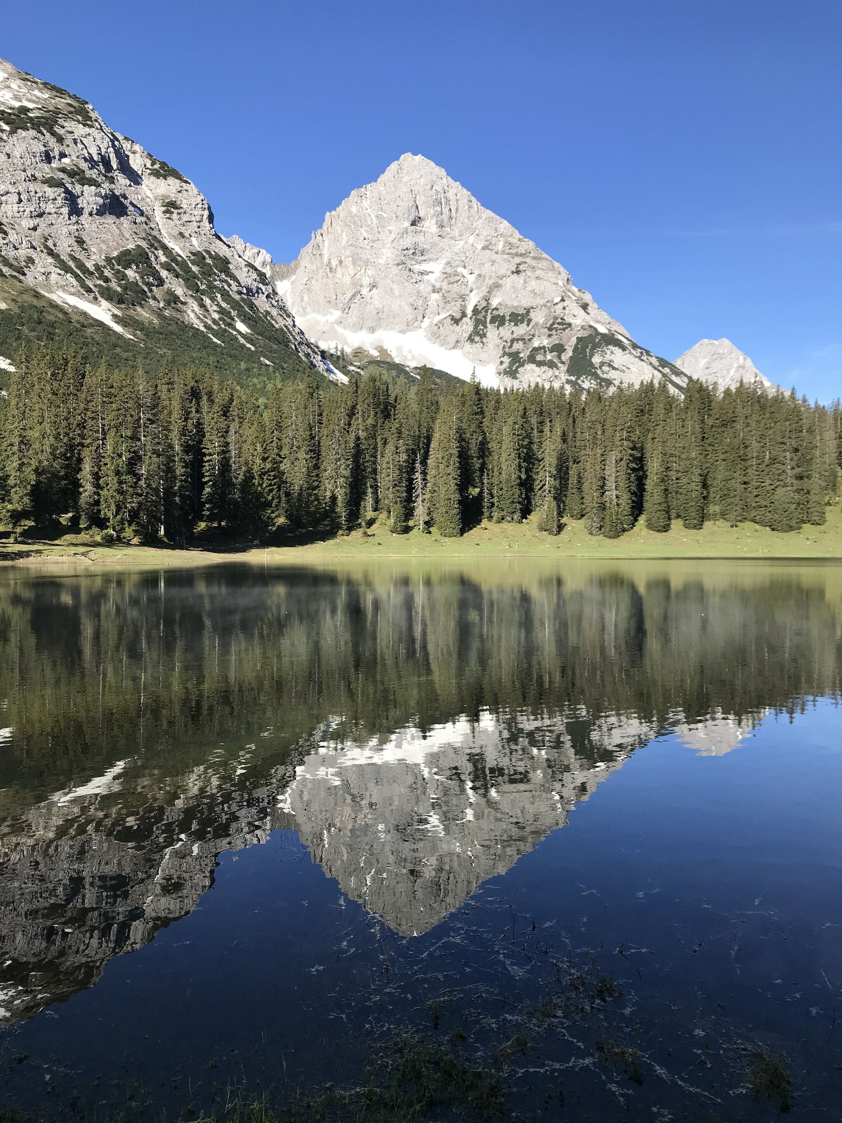 A mountain lake with clear reflections, surrounded by dense forests and rocky mountains.