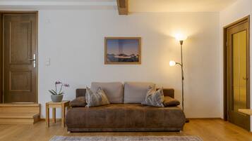 Una sala de estar acogedora con un sofá marrón, una mesita auxiliar con una planta, un cuadro enmarcado en la pared y una lámpara de pie alta.