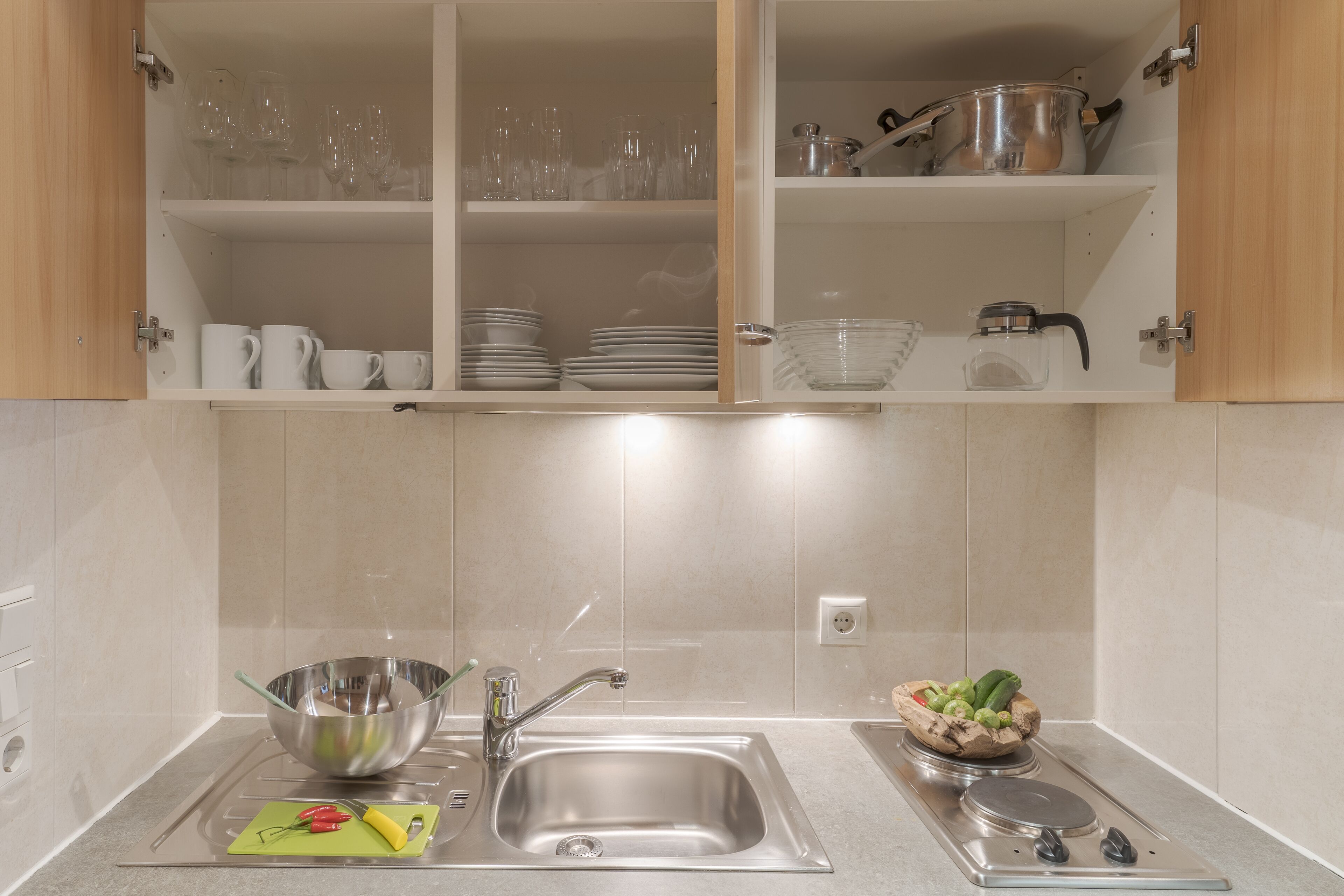 Una cocina con un fregadero de acero inoxidable, una tabla de cortar con vegetales y una olla en la estufa.