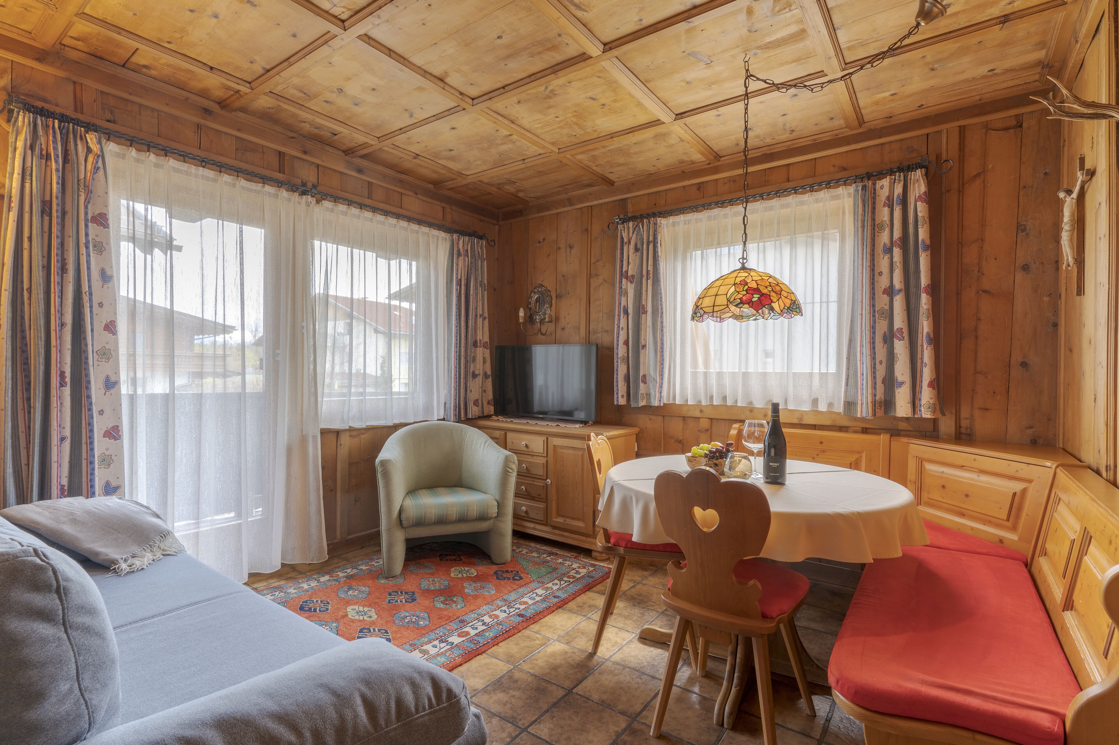 A cozy room with wooden walls and ceiling, a television, a dining table with chairs, and a sofa.