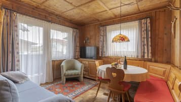 A cozy room with wooden walls and ceiling, a television, a dining table with chairs, and a sofa.