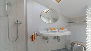 A modern bathroom with a shower, a sink, a mirror, and a glass shelf.