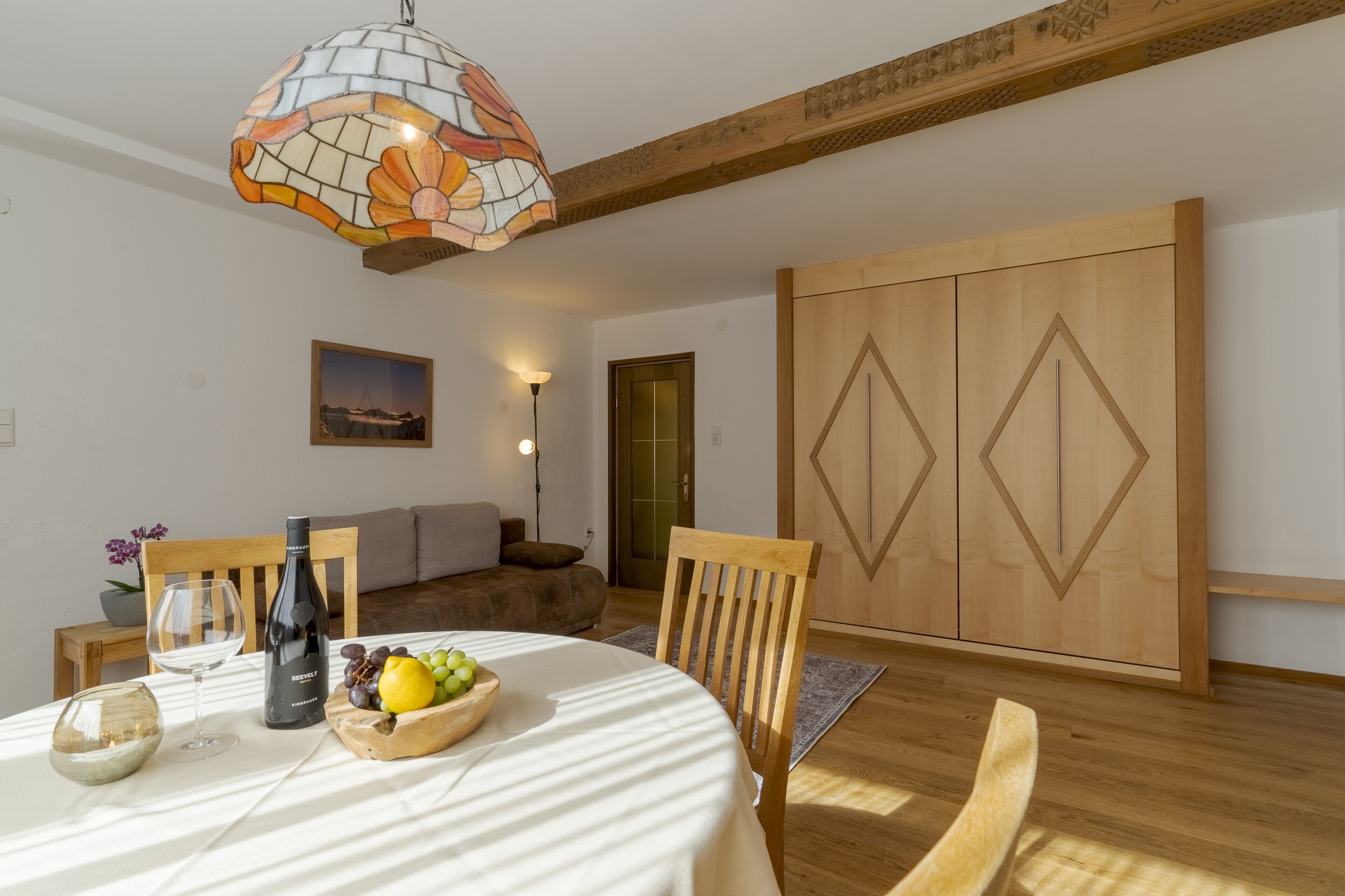 A dining area with a round table, chairs, a wine bottle, and a fruit bowl.