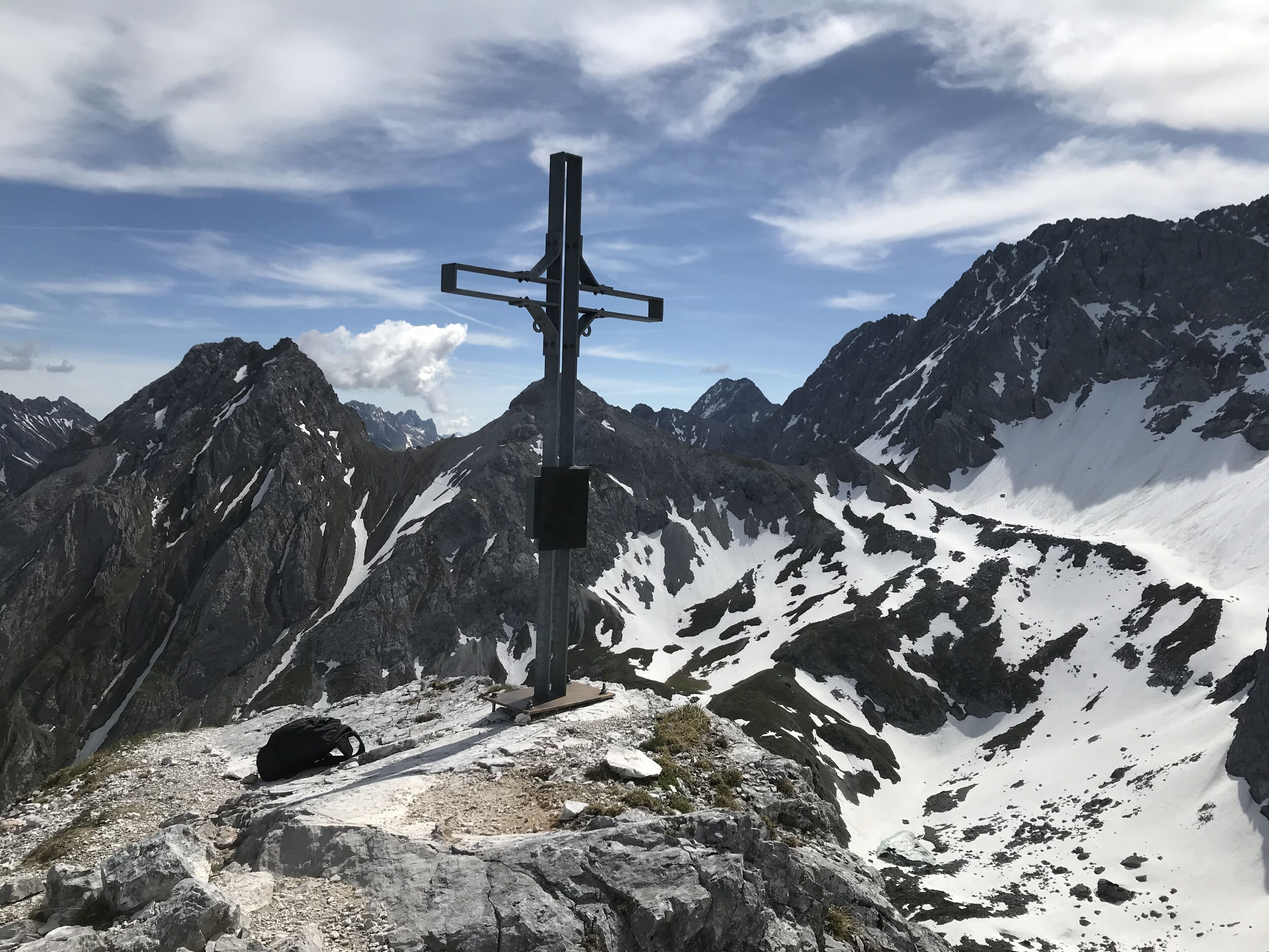 Un pico montañoso con una estructura en forma de cruz, terreno rocoso y parches de nieve.