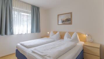 Un lit bien fait, avec du linge de lit blanc, une tête de lit en bois et une table de chevet avec une lampe.