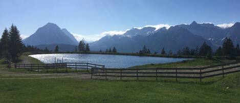 A serene lakeside view with a wooden fence, a clear sky, and mountains in the background.