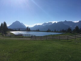 Una vista tranquila de un lago con una valla de madera, cielo despejado y montañas al fondo.